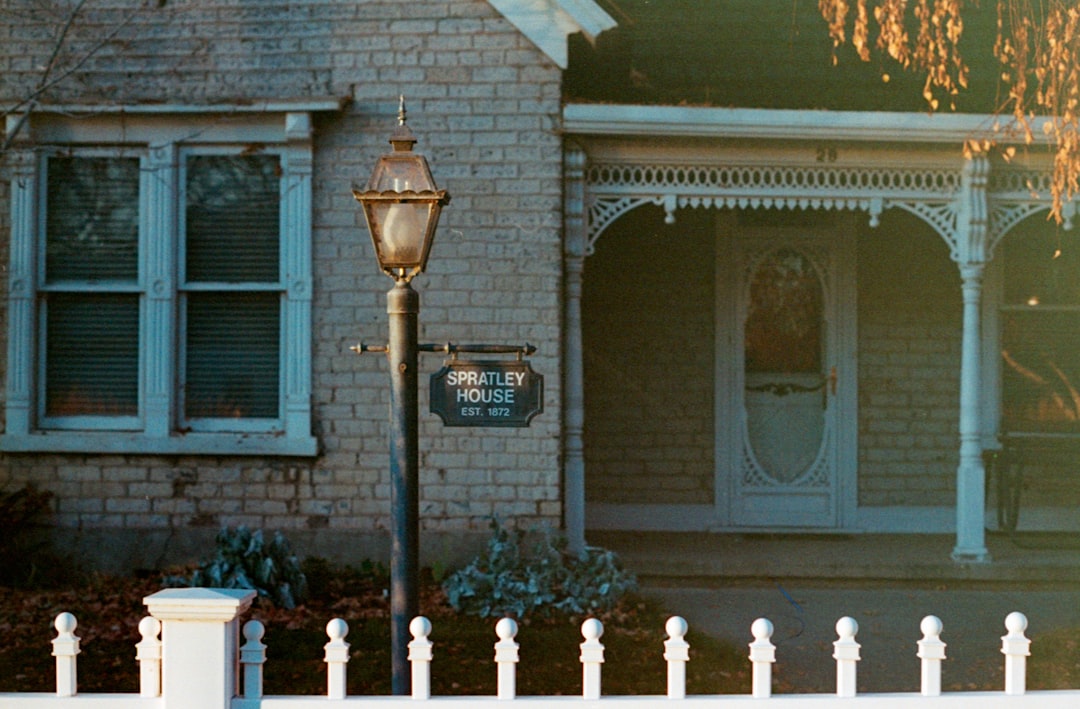 An older two story home with a porch, lamp post and white picket fence