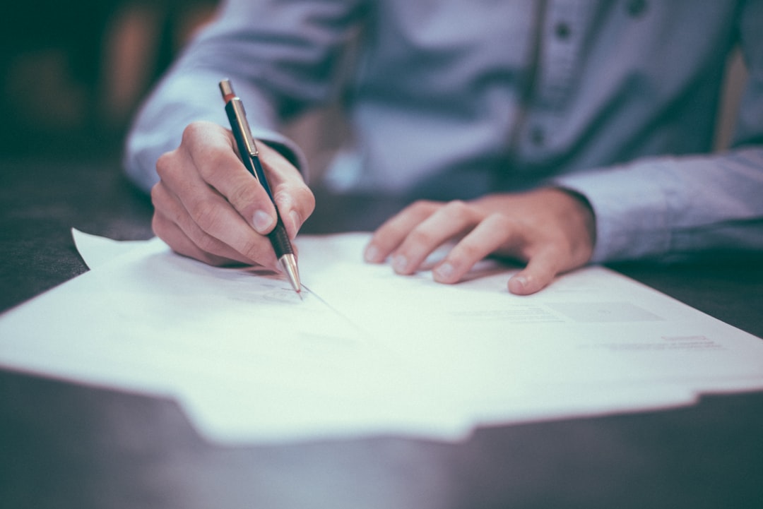 A seller's hand signing a listing agreement at a desk