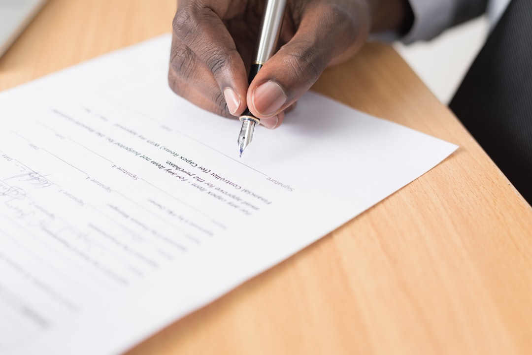 A hand signing a printed agreement with a fountain pen on a wooden desk